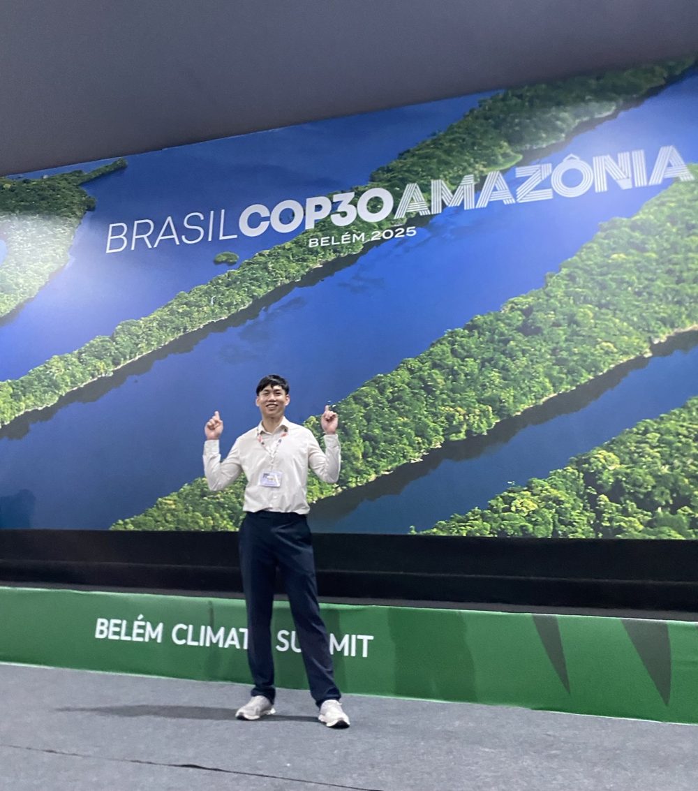 The author posing in front of the conference banner that reads Brasil COP30 Amazônia, Belém 2025
