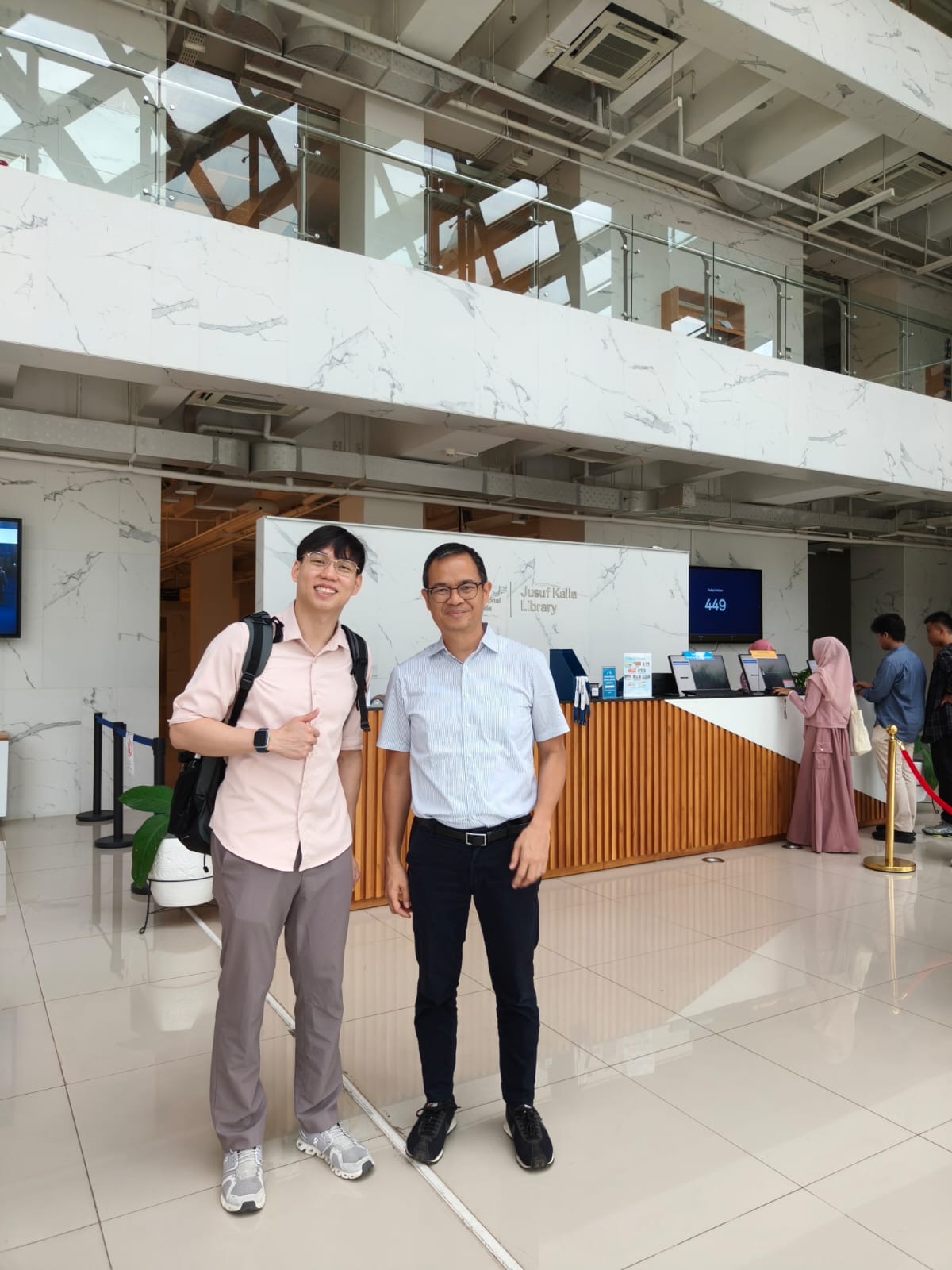 The author standing with Dr. Sonny Mumbunan in an institutional library lobby in Jakarta, Indonesia